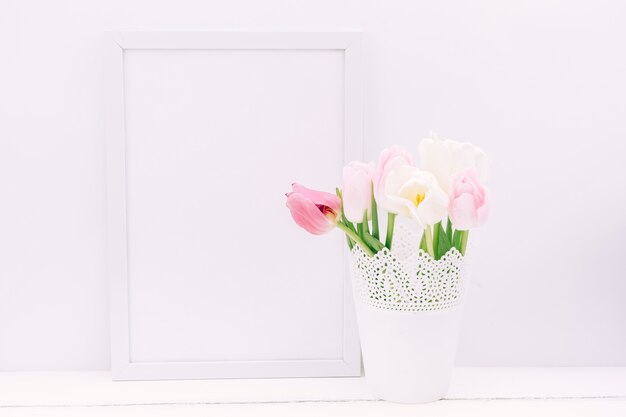 Flores frescas de tulipán en florero con marco de fotos en blanco