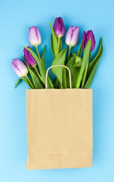 Flores frescas de tulipán púrpura en papel marrón sobre superficie azul