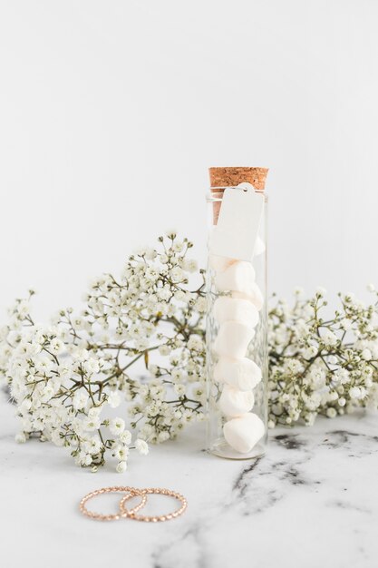 Flores de gypsophila; Anillos de boda y malvavisco en tubo de ensayo sobre fondo blanco