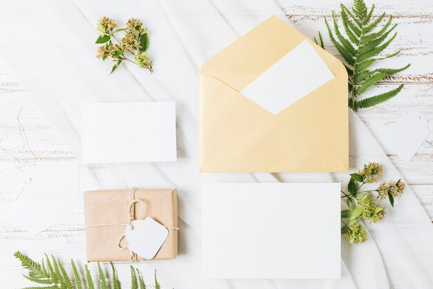 Flores; helecho; caja de regalo envuelta; tarjeta; Sobre y bufanda en mesa de madera.