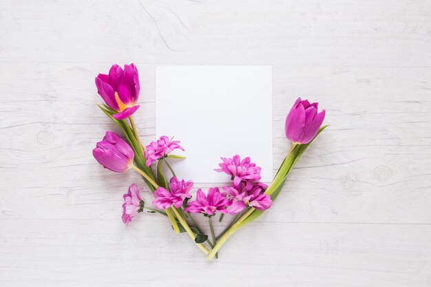 Flores moradas con papel en blanco sobre mesa.