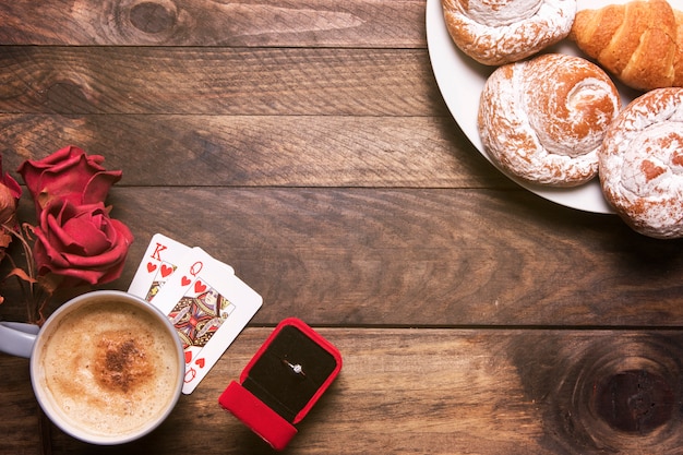 Foto gratuita flores, panadería en platos, anillo en caja de regalo, naipes y taza de bebida.