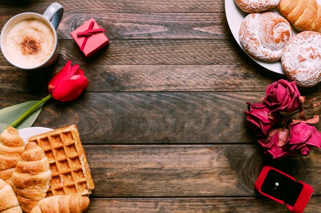 Flores, panadería en platos, anillo en caja de regalo y taza de bebida.