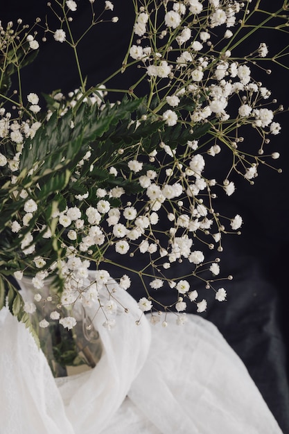 Foto gratuita flores con plantas en jarrón cerca de textil blanco.