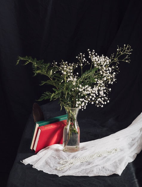 Flores con plantas en jarrón cerca de volúmenes y cuentas en textil blanco sobre mesa