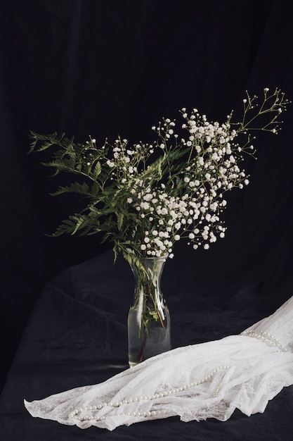 Flores con plantas en jarrón junto a cuentas en textil blanco.