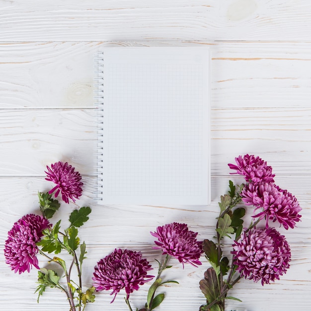 Flores púrpuras con cuaderno en blanco en mesa de madera