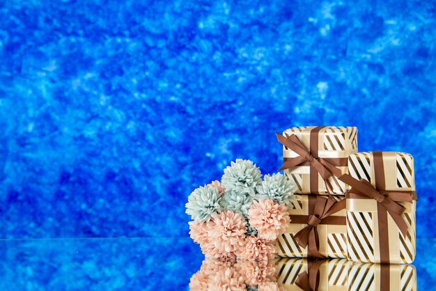 Flores de regalos navideños de vista frontal reflejadas en el espejo sobre fondo azul borroso