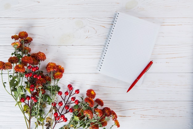 Flores rojas con cuaderno en blanco y pluma en mesa de madera