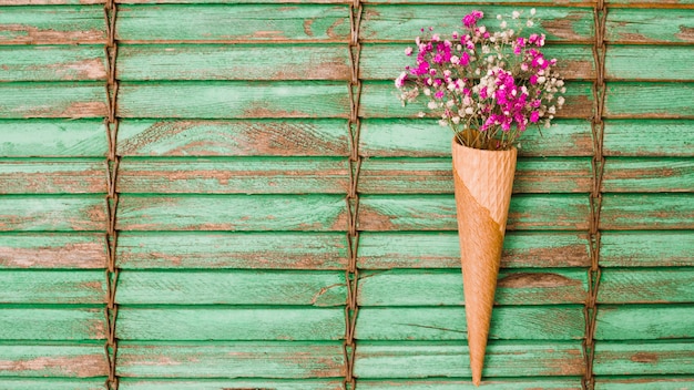 Flores rosadas de aliento de bebé dentro del cono de waffle contra persianas de madera