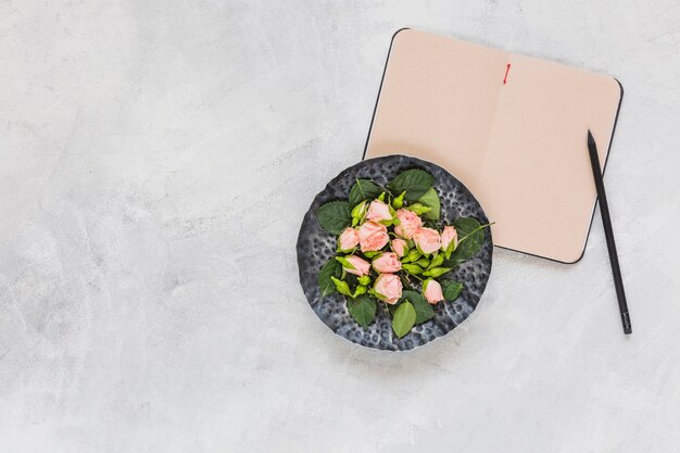 Flores rosadas en bandeja circular con diario y lápiz sobre fondo concreto