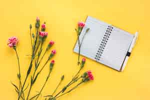 Foto gratuita flores rosas con cuaderno en blanco en mesa