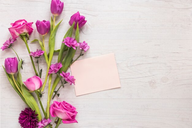 Flores rosas con papel en blanco sobre mesa de madera.