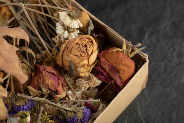 Flores de rosas secas con hojas secas en una caja de papel.