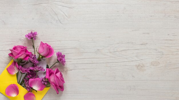 Flores rosas en sobre en mesa de madera