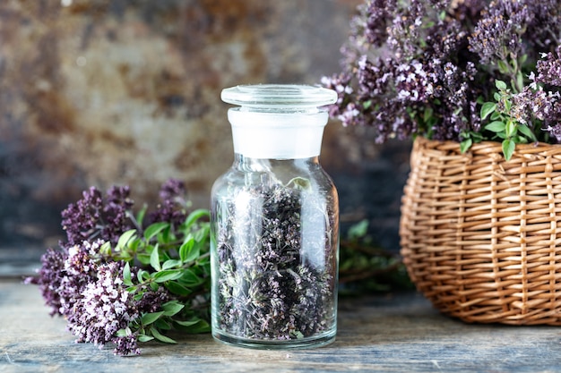 Flores secas de orégano en una botella de vidrio sobre una mesa de madera.