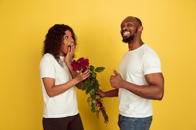 Flores para sonreír. Celebración del día de San Valentín, feliz pareja afroamericana aislada sobre fondo amarillo de estudio. Concepto de emociones humanas, expresión facial, amor, relaciones, vacaciones románticas.