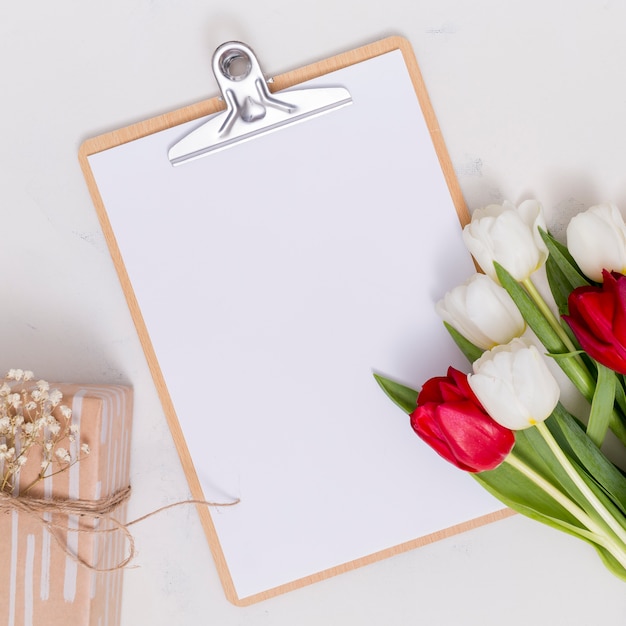 Foto gratuita flores de tulipán blanco y rojo; caja de regalo; papel blanco en blanco; con portapapeles sobre aislado sobre fondo blanco