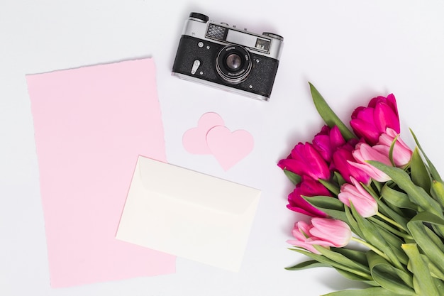 Flores de tulipán; camara retro forma de corazón; y papel en blanco contra aislado sobre fondo blanco