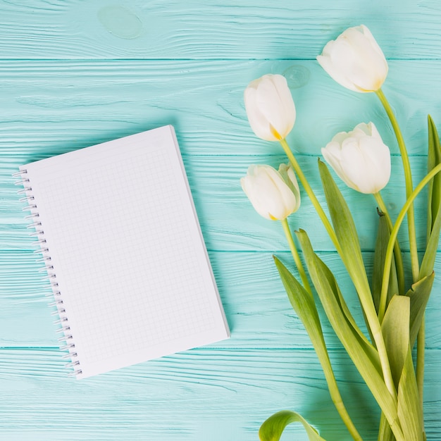 Flores de tulipán con cuaderno en blanco en mesa de madera