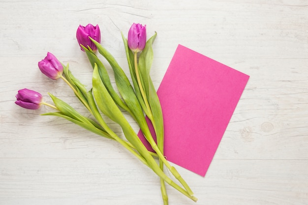 Foto gratuita flores de tulipán morado con papel sobre mesa