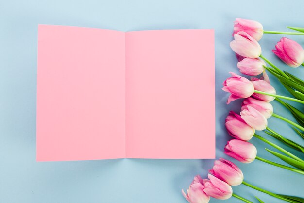 Flores de tulipán con papel en blanco sobre mesa