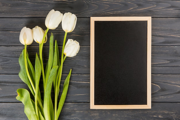 Flores de tulipán con pizarra en blanco en la mesa de madera