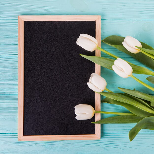 Flores de tulipán con pizarra en blanco en la mesa