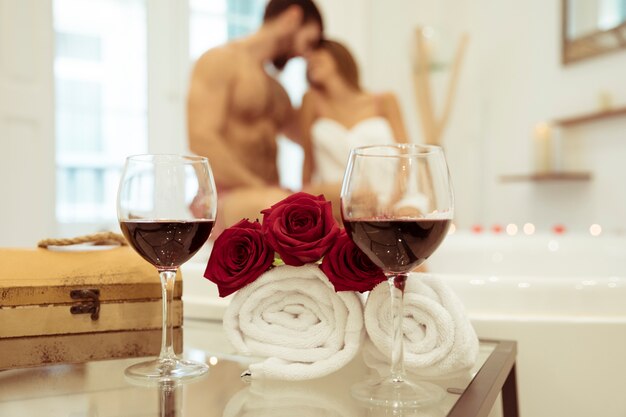 Flores y vasos de bebida cerca de pareja besándose en la bañera de hidromasaje