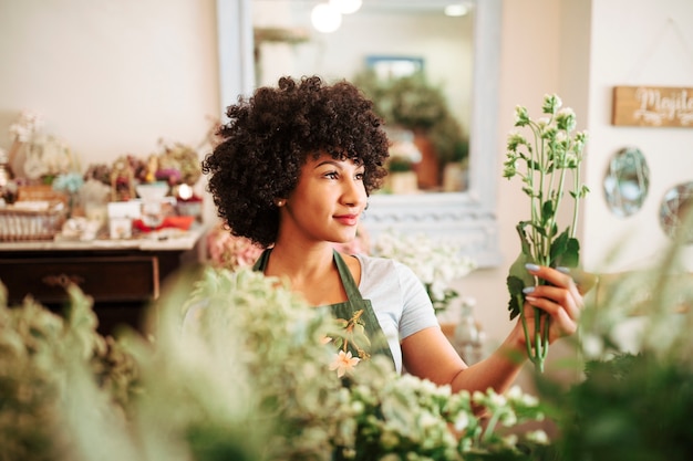 Foto gratuita florista afroamericana que mira el manojo de flores blancas