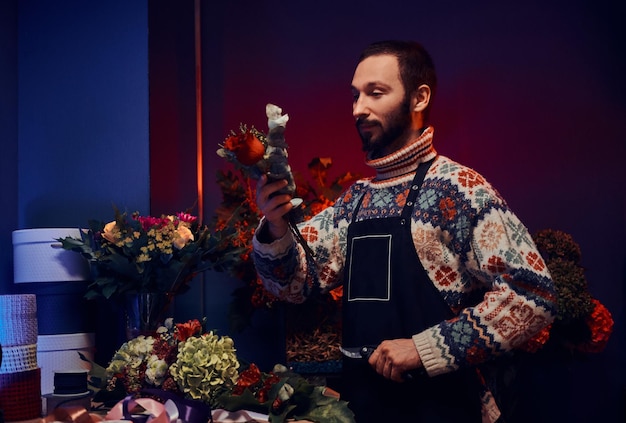 El florista barbudo experimentado está creando un bonito ramo usando una variedad de flores.