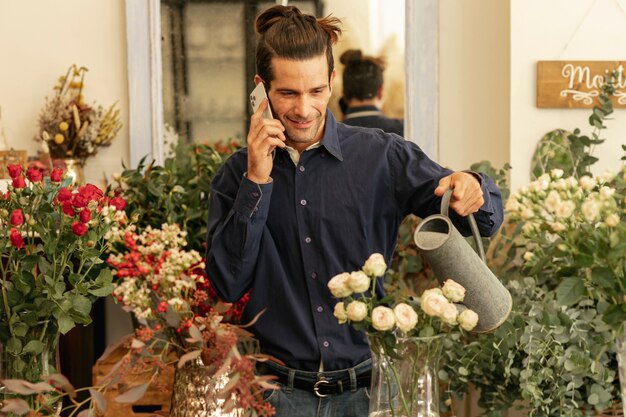 Florista experimentado hablando por teléfono y regando las plantas