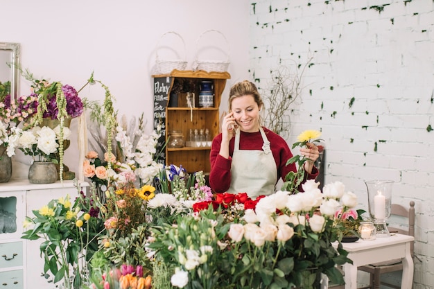 Florista hablando en el teléfono inteligente y recogiendo flores
