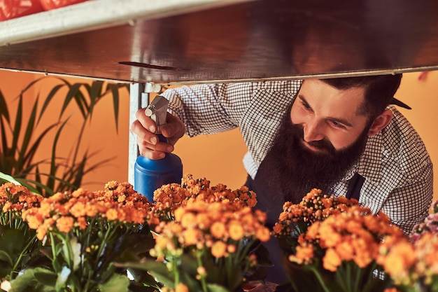 Florista masculino profesional con barba y tatuaje en la mano usando uniforme cuidando flores en una floristería moderna.