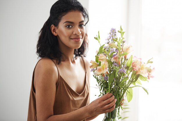 Florista de sexo femenino africano hermoso que sonríe haciendo el ramo de flores.