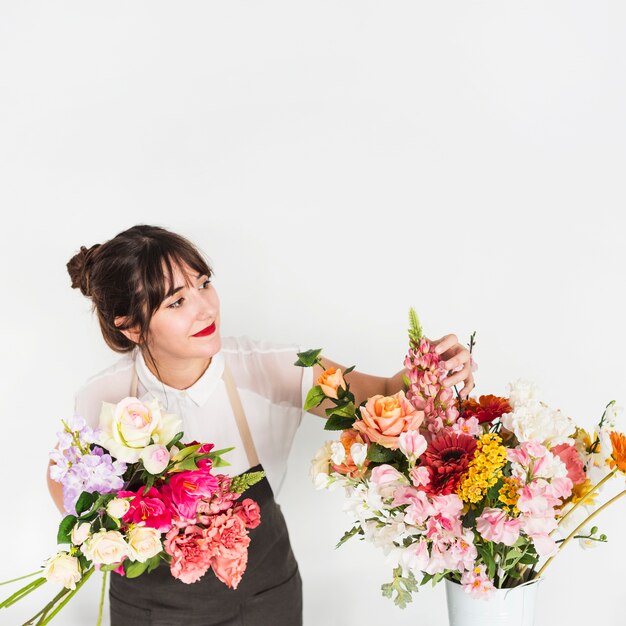 Florista de sexo femenino que mira las flores en el fondo blanco