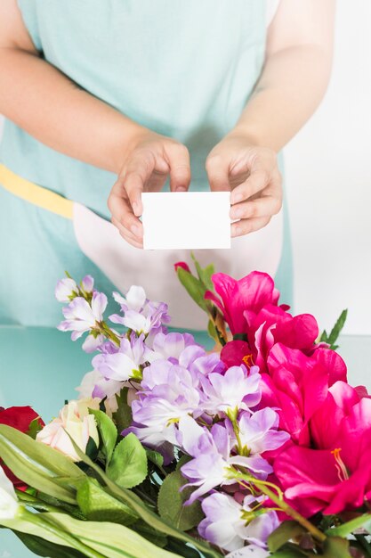 Florista de sexo femenino que sostiene la tarjeta de visita en blanco sobre el manojo de flores frescas