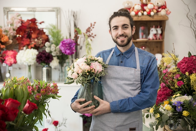 Florista de sexo masculino joven feliz que sostiene el florero disponible que se coloca en la floristería