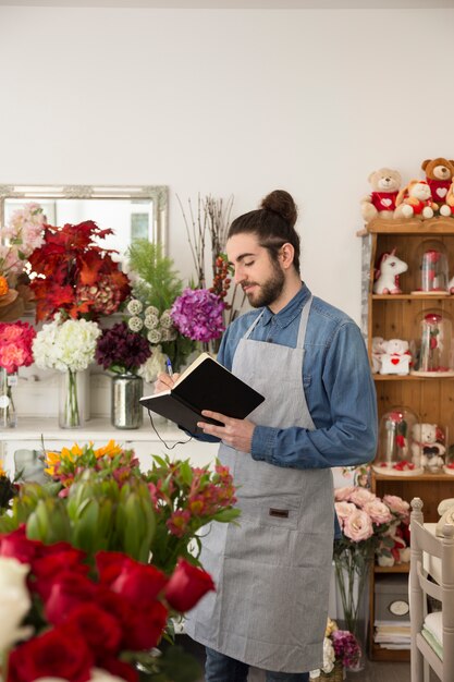 Florista de sexo masculino joven que se coloca en la tienda de flores que escribe en el diario con la pluma