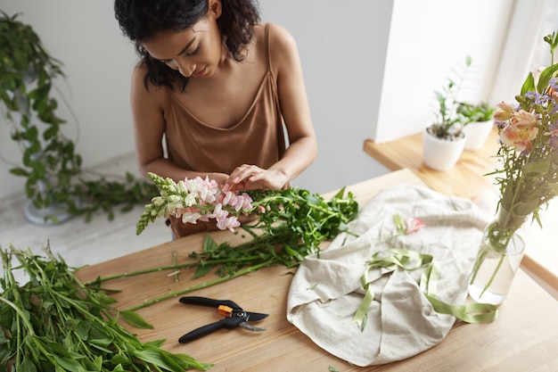 Floristería africana hermosa joven que cuida las flores en el lugar de trabajo.