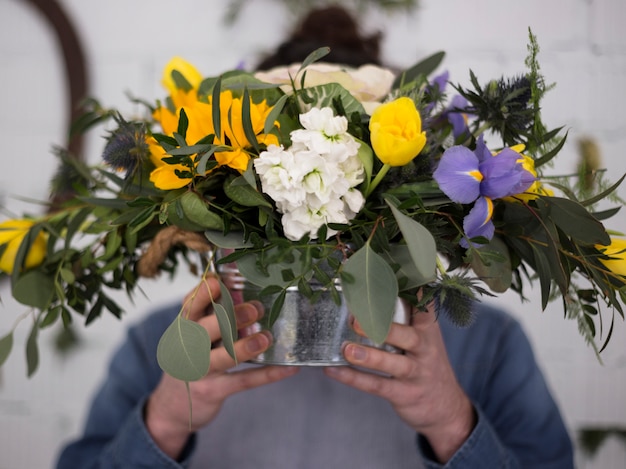 Floristería Defocused sosteniendo un jarrón de flores frente a su cara