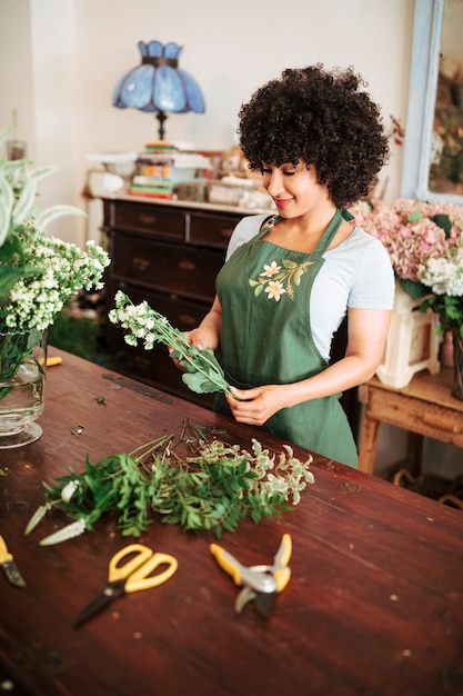 Floristería femenina africana feliz que mira el manojo de flores blancas en tienda