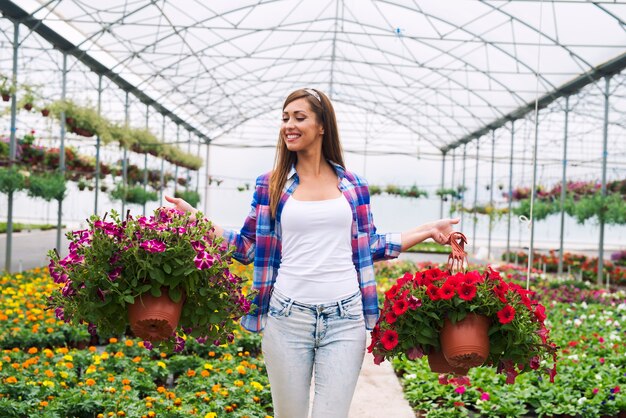 Floristería femenina llevando plantas de flores en macetas en invernadero organizarlos para la venta