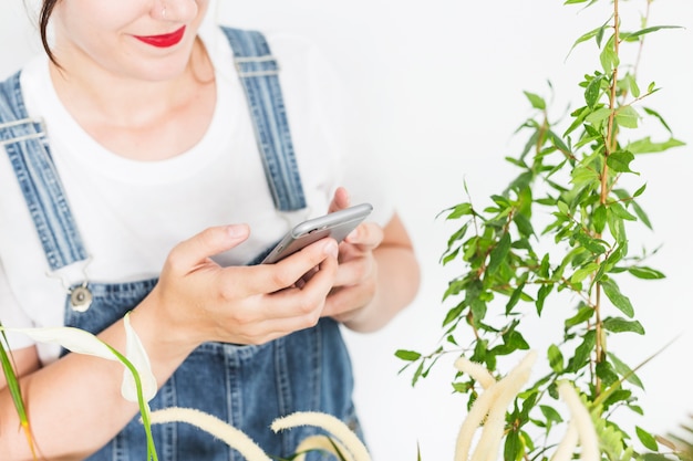 Foto gratuita floristería femenina utilizando un teléfono móvil cerca de las plantas.