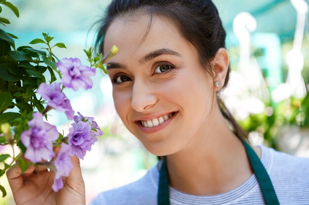 Floristería hermosa joven posando, sonriendo entre flores.