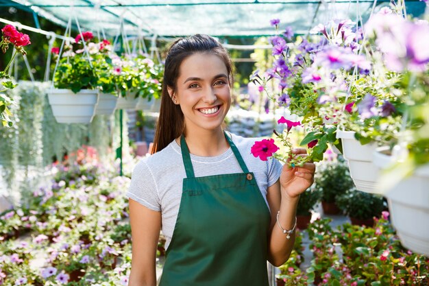 Floristería hermosa joven posando, sonriendo entre flores.