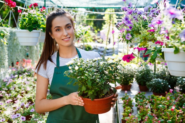 Floristería hermosa joven posando, sonriendo entre flores.