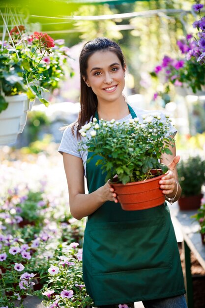 Floristería hermosa joven posando, sonriendo entre flores.