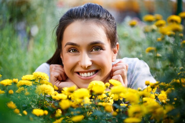 Floristería hermosa joven posando, sonriendo entre flores.