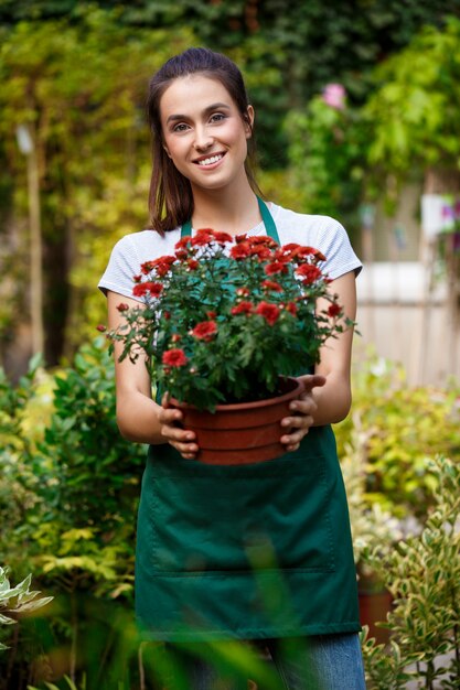 Floristería hermosa joven posando, sonriendo entre flores.